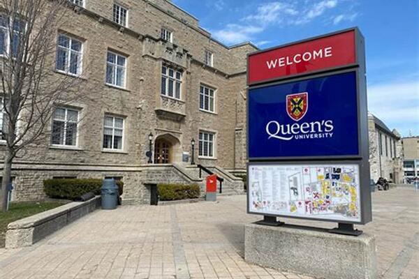 Sign reading "Welcome, Queen's University" in front of a limestone campus building