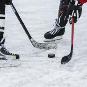 Image of two hockey sticks surrounding one puck, with two skates on the ice - like in a face-off in hockey